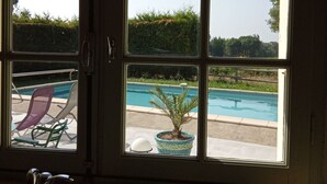 Ein Fenster mit Blick auf einen Swimmingpool, Liegestühle und einen Blumentopf.
