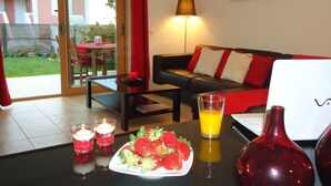 Una sala de estar moderna con una mesa de vidrio, un sofá con cojines rojos, una lámpara y vistas al exterior.