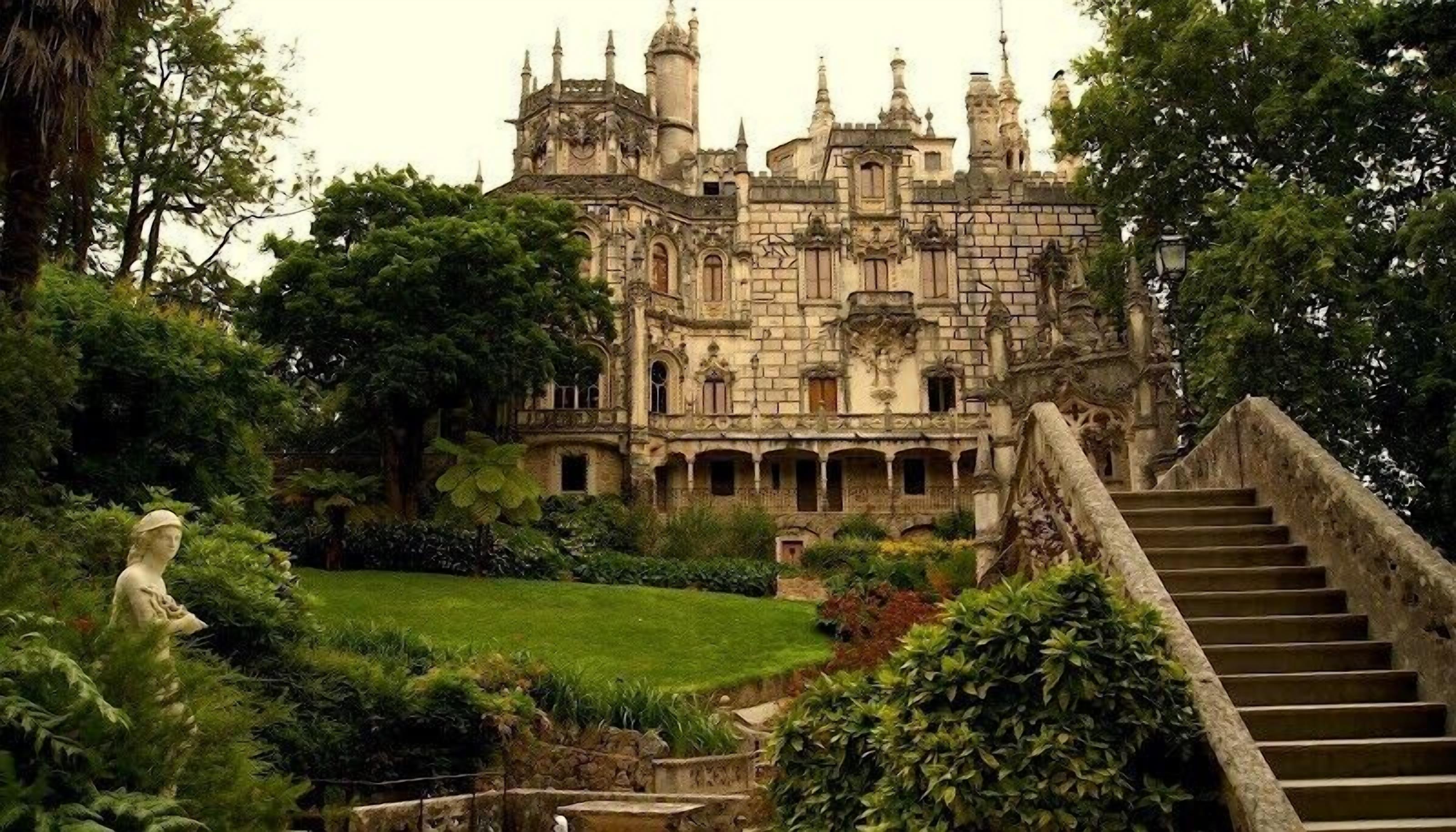 A historic castle with a large courtyard, a central staircase, and lush greenery.