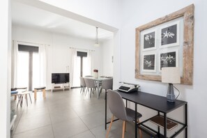 Una sala moderna con televisor de pantalla plana, un comedor con mesa y sillas, y un espacio de trabajo con escritorio y silla.
