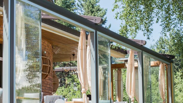 A modern outdoor seating area with glass walls, wooden furniture, and a brick wall. - Family Hotel Saint George (Sofia)