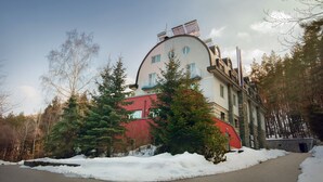 A multi-story building with a curved facade, surrounded by snow-covered ground and trees. - Family Hotel Saint George (Sofia)