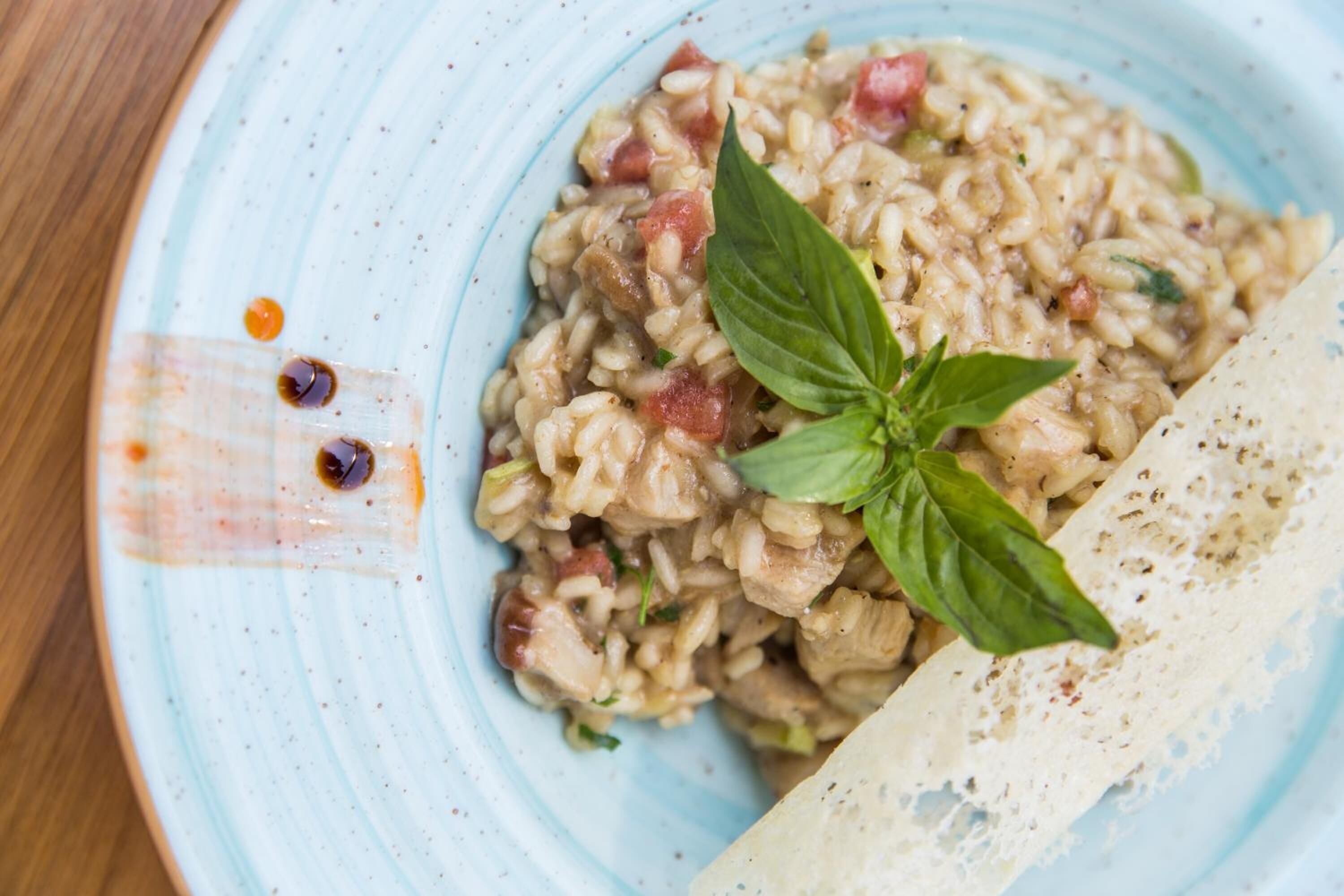 Een bord risotto met basilicum garnering en een stukje brood ernaast.
