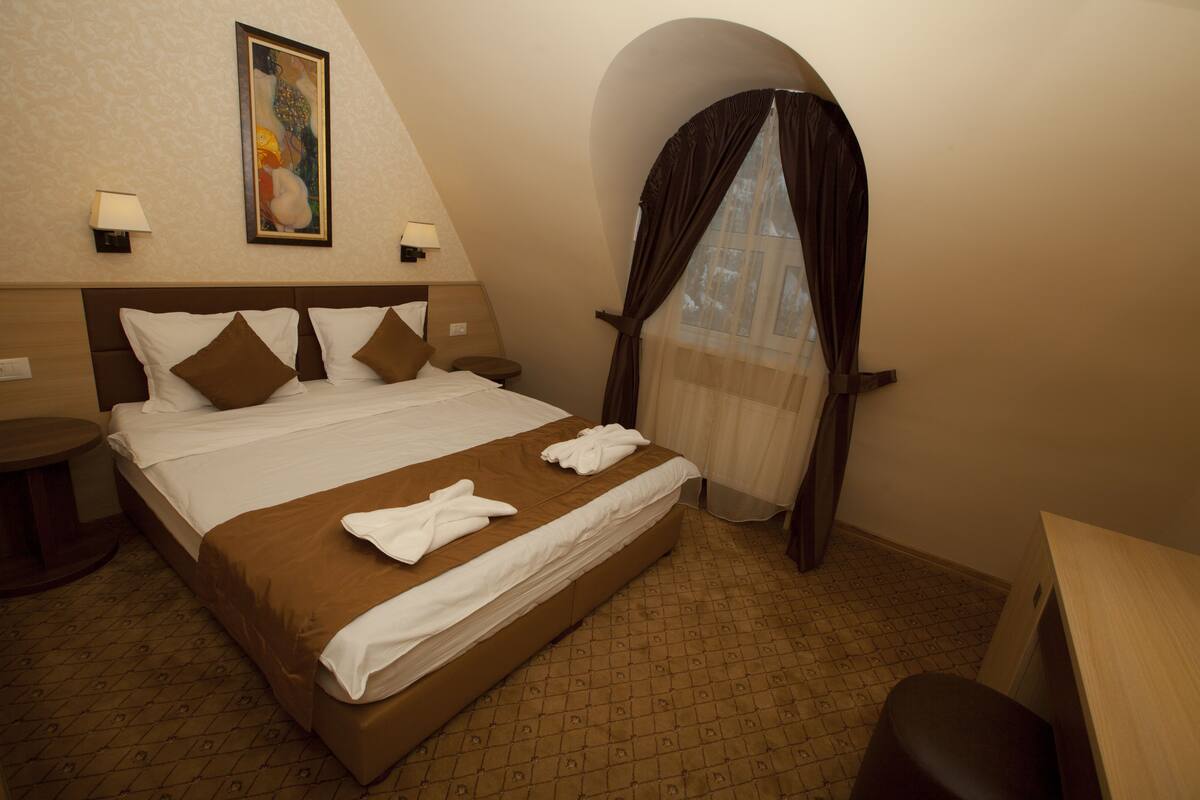 Hotelkamer met een groot bed, nachtkastje, lamp, schilderij aan de muur en raam met gordijn.