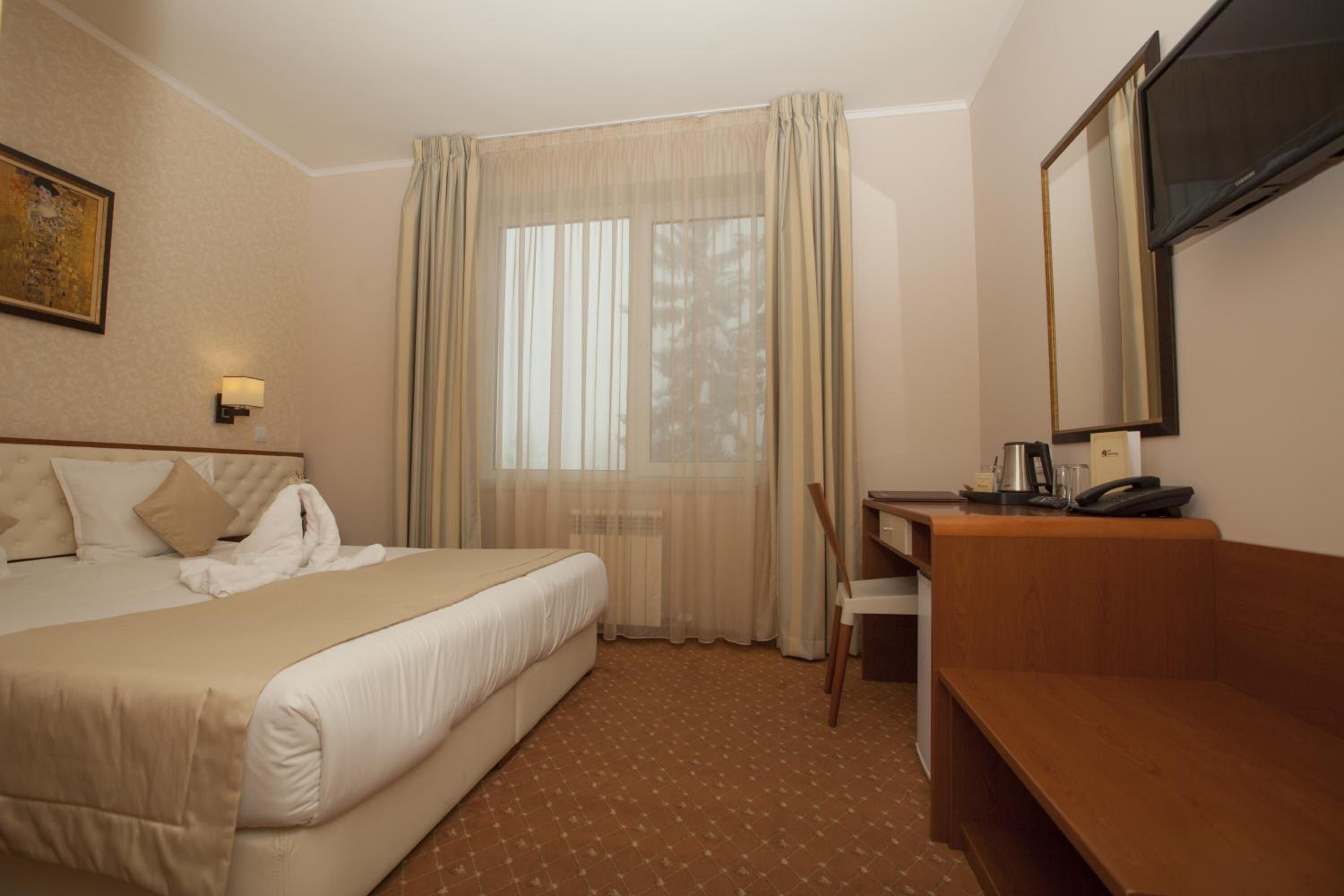 Una habitación de hotel con cama, escritorio, silla, televisor y ventana con cortinas.