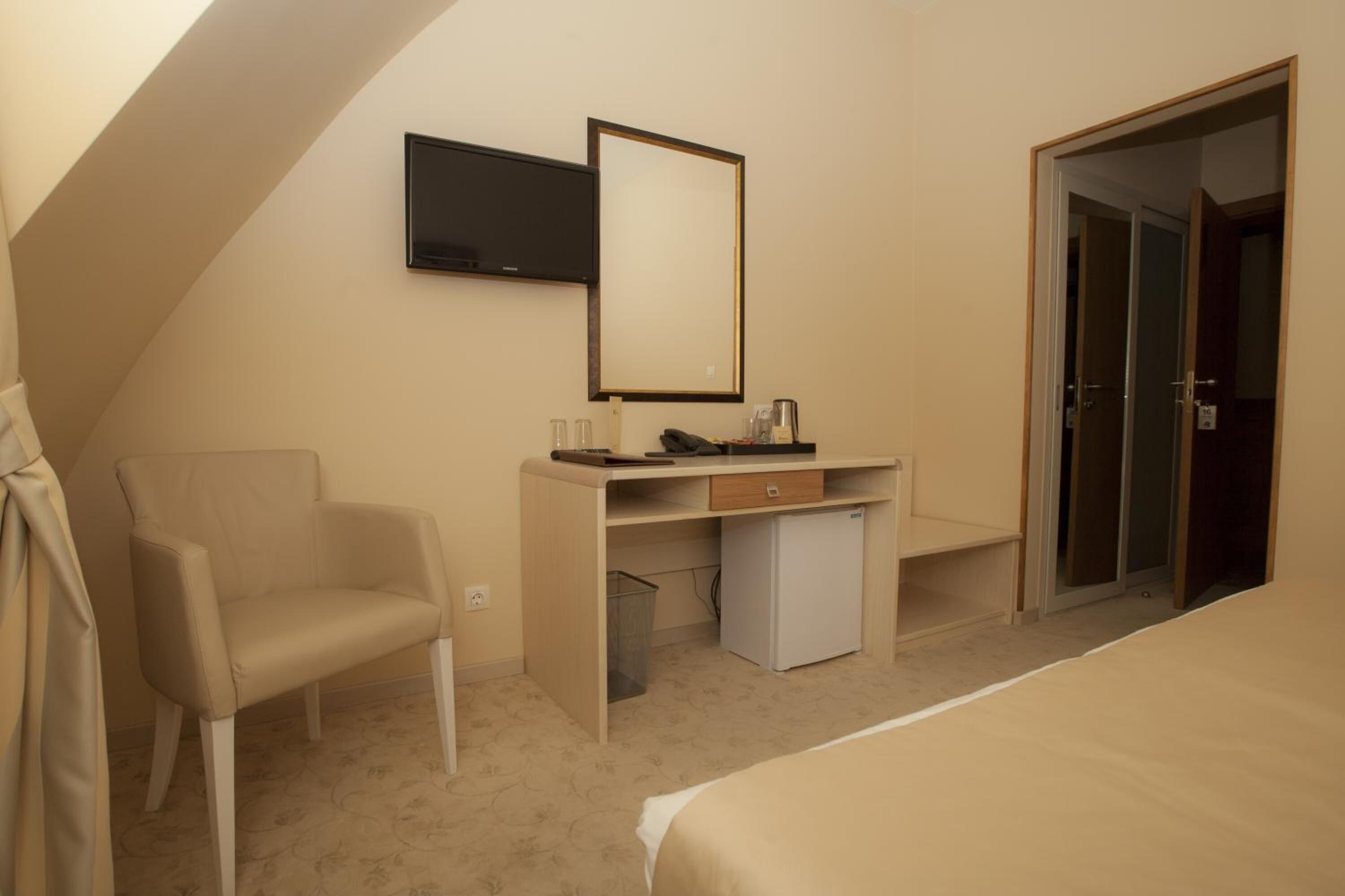 A hotel room with a bed, a desk with a chair, a television, and a wardrobe.