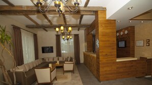 A modern reception area with a wooden reception desk, a seating area with a sofa and chairs, and a chandelier. - Family Hotel Saint George (Sofia)