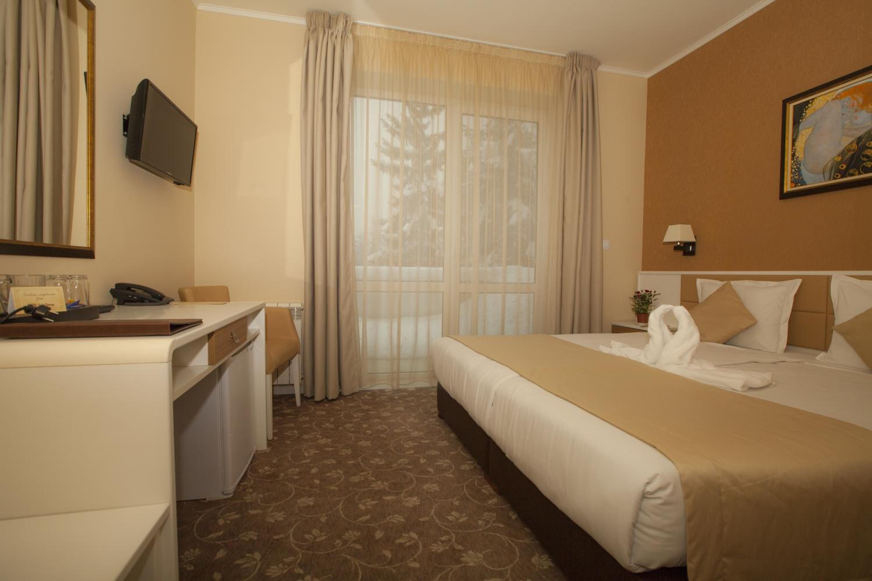 A hotel room with a bed, a desk, a chair, a television, and a window with curtains.