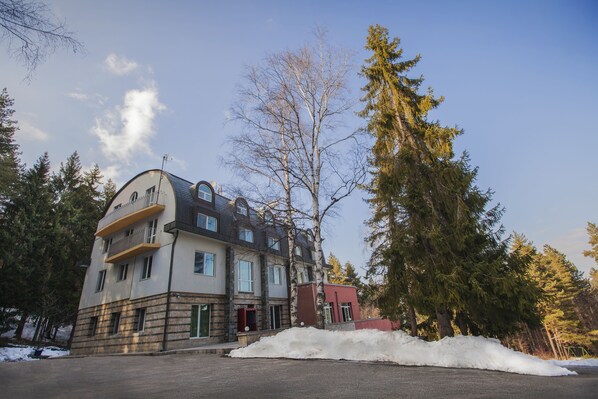 Un edificio de varios pisos con balcones, rodeado de árboles y un suelo cubierto de nieve.