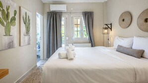 A bedroom with a bed, two wall-mounted air conditioners, a ceiling light, a window with curtains, and a door leading to another room.