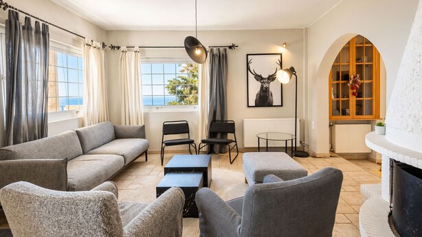 A modern living room with a sofa, chairs, a coffee table, a fireplace, and a large window with curtains.