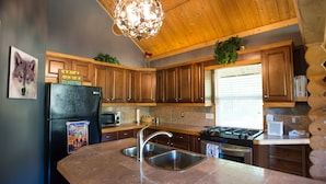 A kitchen with wooden cabinets, a black refrigerator, a stainless steel sink, a gas stove, and a wooden ceiling. - Cozy Log Home -King bed, full kitchen, bathroom with clawfoot tub, outdoor area  (Talkeetna)