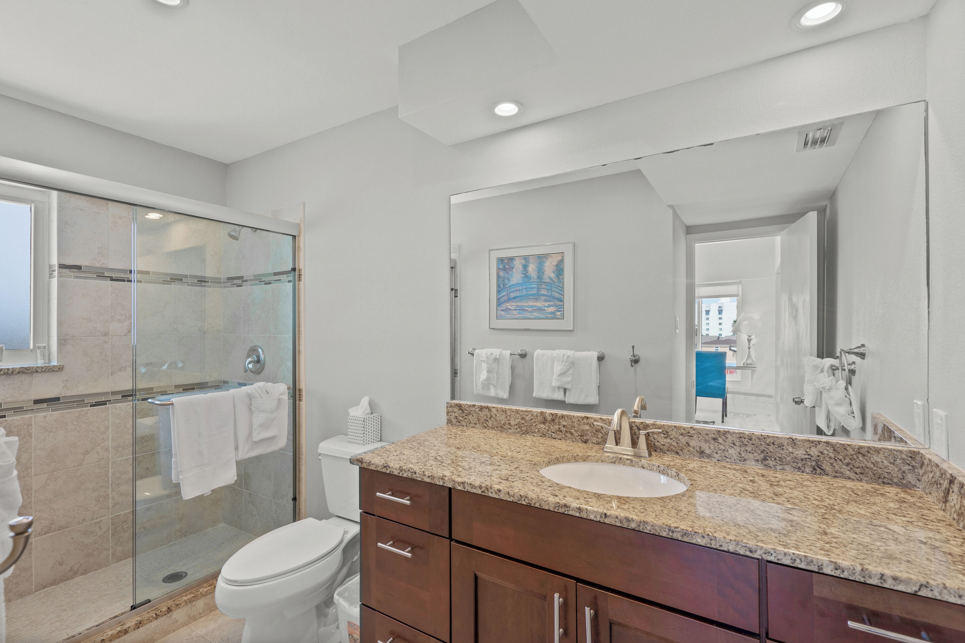 A modern bathroom with a glass shower enclosure, a white toilet, a granite countertop sink, and wooden cabinets.