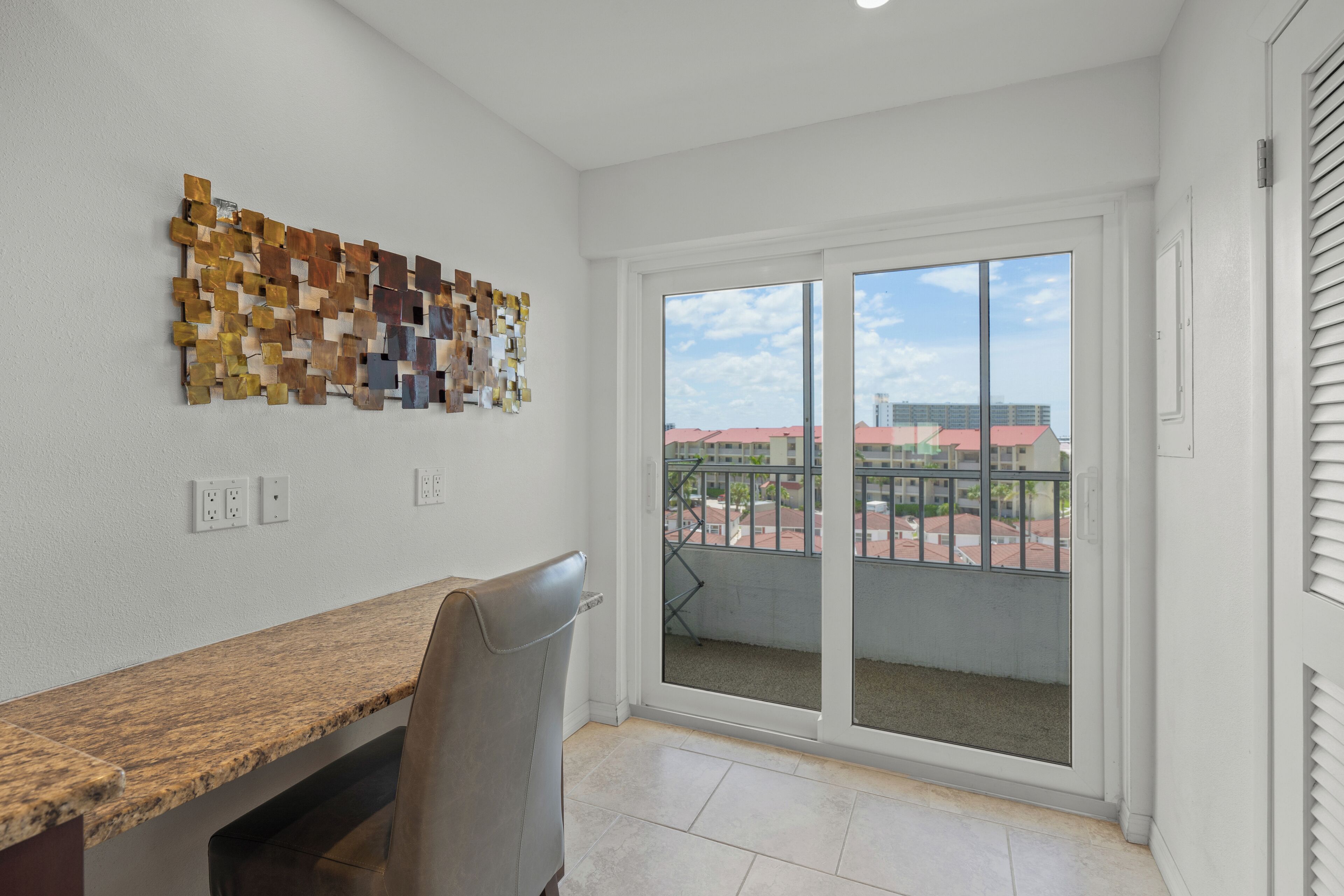 A room with a granite countertop, a chair, a wall art piece, and a sliding glass door leading to an outdoor balcony.