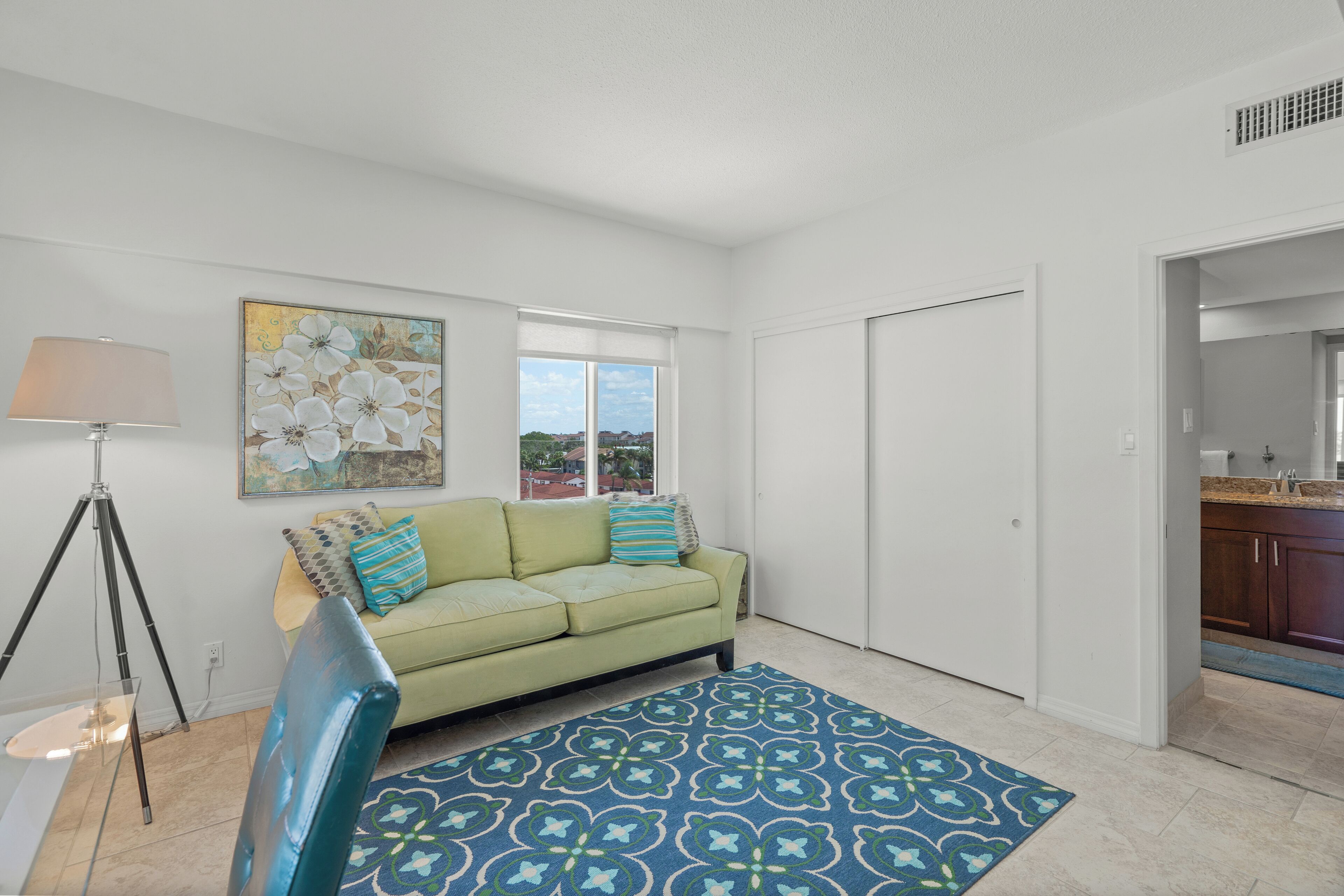 A living room with a green sofa, a patterned rug, a floor lamp, and a painting on the wall.