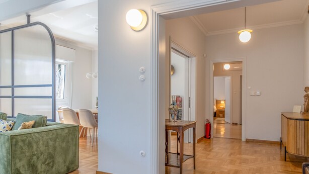 A spacious living area with a green sofa, wooden flooring, and a dining table with chairs.