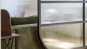 A room with a green upholstered sofa, a wooden table, and a decorative shelf with items.
