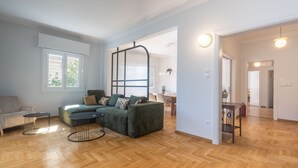 A spacious living room with a green sofa, two black coffee tables, and a wooden herringbone floor.