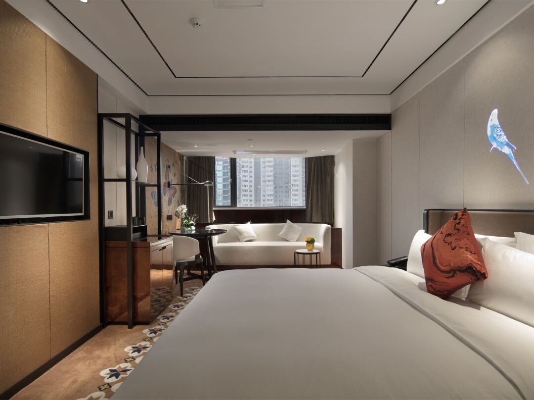 A modern hotel room with a large bed, a sofa, a desk, and a TV.