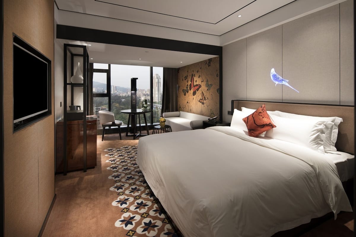 Une chambre d’hôtel avec un grand lit, un bureau avec une chaise, une petite table avec une chaise et un téléviseur fixé au mur.