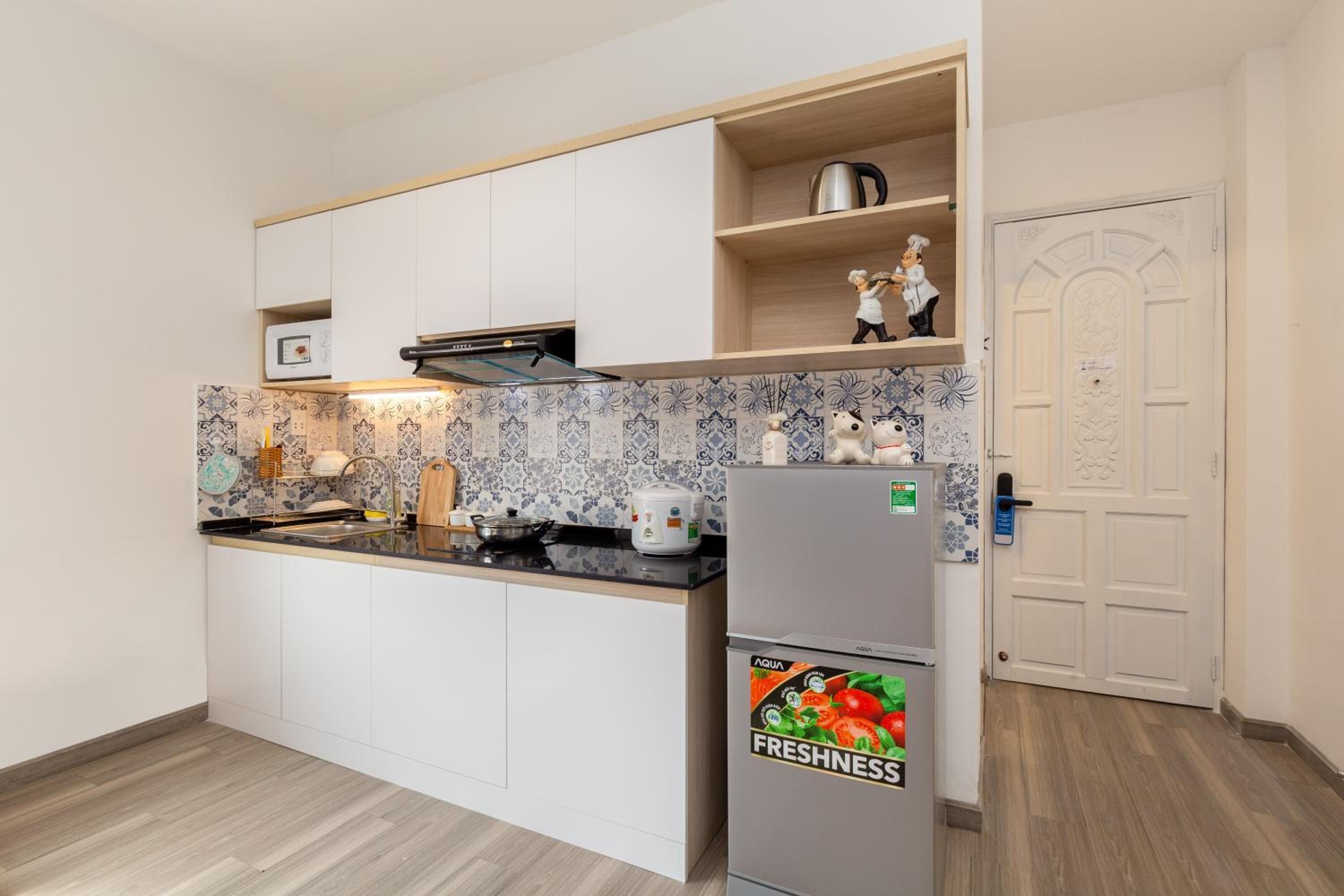 A compact kitchen with white cabinets, a black countertop, and a refrigerator with a fresh produce sticker.