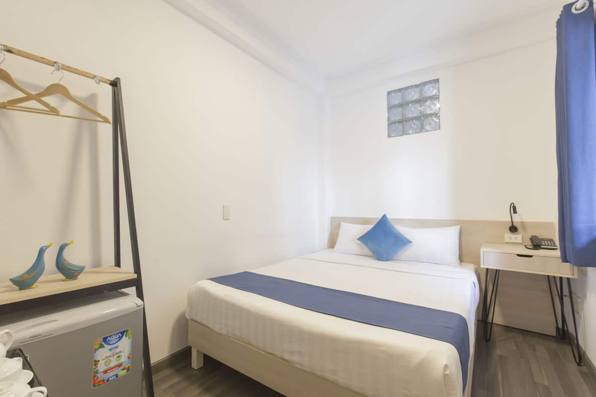 A hotel room with a bed, a desk, a small refrigerator, and a window with a view.