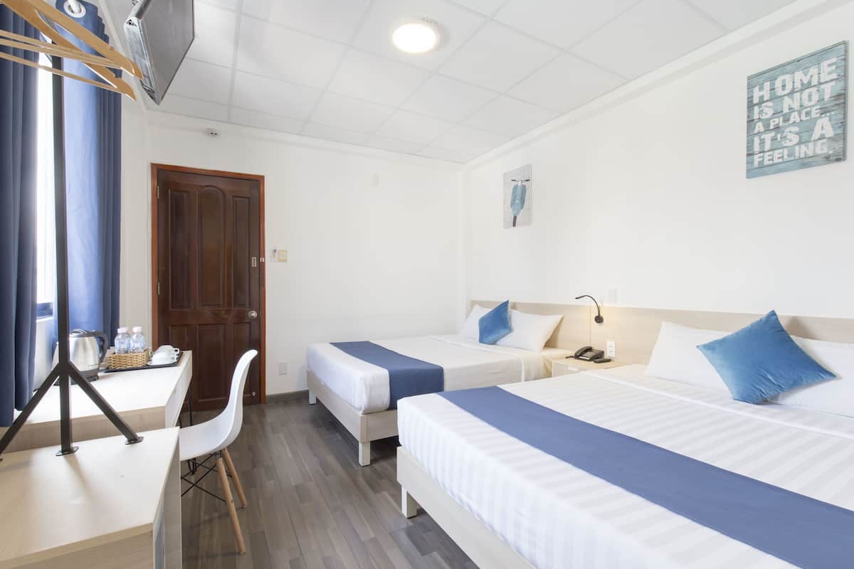 A hotel room with two beds, a desk, and a chair. There is a door, a wall clock, and a sign that says "HOME IS NOT A PLACE, IT'S A FEELING."