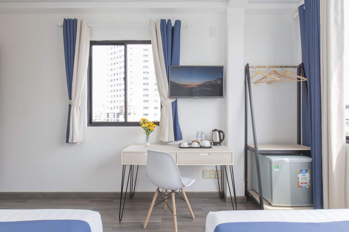 A hotel room with a bed, a desk with a chair, a small refrigerator, a television, and a window with curtains.