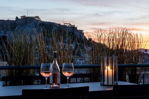 Ein Tisch mit zwei Weingläsern und einer Flasche, einer Kerze und Blick auf ein historisches Gebäude bei Sonnenuntergang.