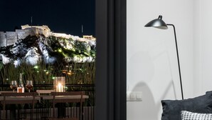 Ein modernes Wohnzimmer mit einer Couch und zwei kleinen Tischen, einer Lampe und Blick auf ein historisches Gebäude bei Nacht.