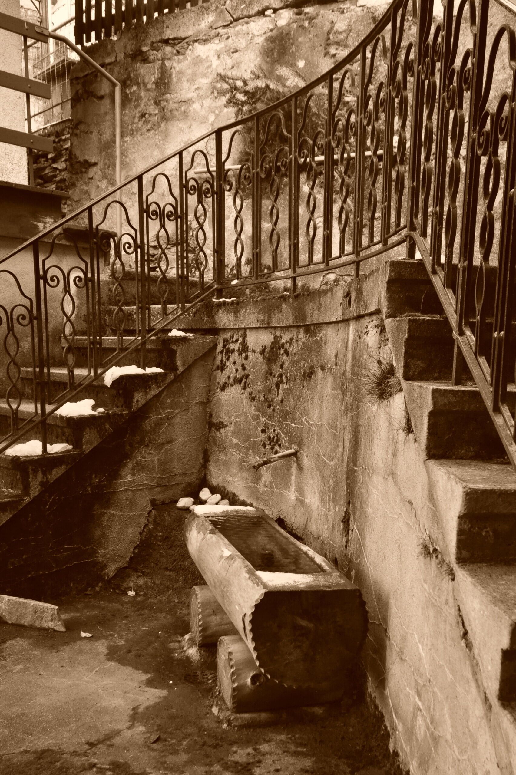 Eine Treppe mit aufwendiger Metallgeländerung und Steinstufen, die zu einer oberen Ebene führt.