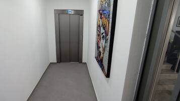 Um corredor estreito com um elevador cinzento e uma pintura abstrata colorida na parede.