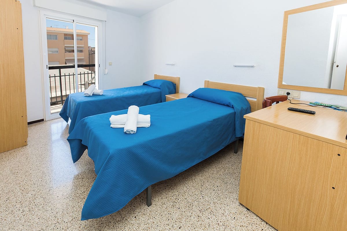A hotel room with two beds, a wooden desk, and a mirror.