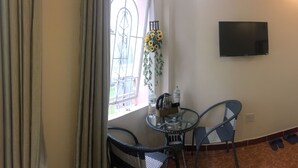 A room with a glass table and two chairs, a TV mounted on the wall, and a window with curtains. - Nguyen Minh Hostel (Cam Ly - Da Lat)