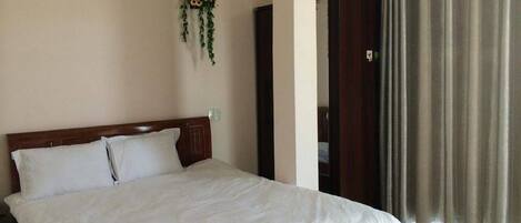 A neatly made bed with a white bedspread and a sunflower decoration, a wooden wardrobe, and a curtain on a window.