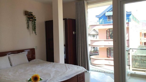 A hotel room with a bed, a view of the outside buildings, and a balcony. - Nguyen Minh Hostel (Cam Ly - Da Lat)
