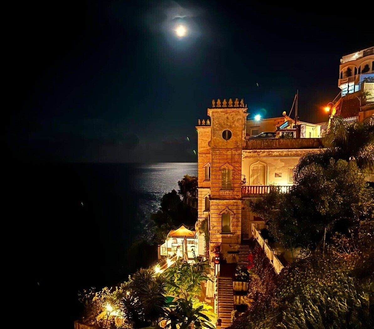 Um edifício histórico com uma torre, com vista para um corpo de água, sob a lua cheia.