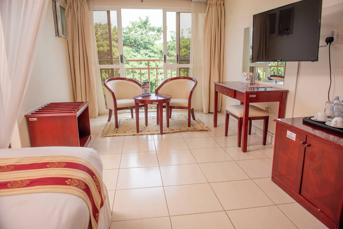 Habitación de hotel con cama, escritorio, dos sillas, televisor y vista a zonas verdes.