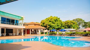 Zona de piscina con sillas de descanso, sombrillas y un edificio con amplias ventanas.