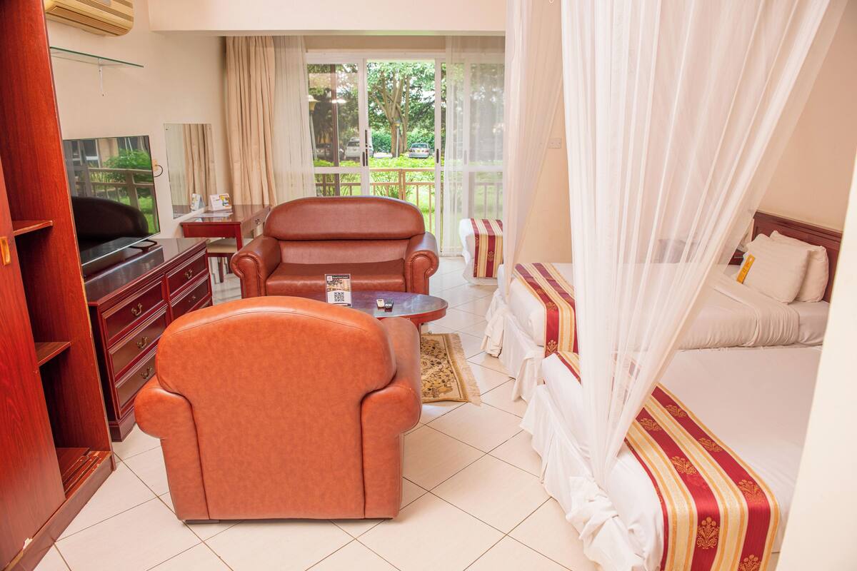 Habitación de hotel con sofá, cama con dosel, televisor y vistas al exterior.