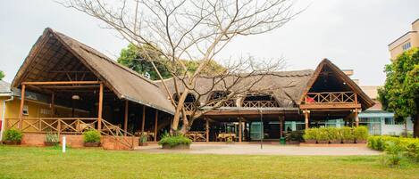 A building with a thatched roof and wooden structure, surrounded by a grassy area and trees.