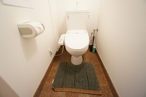 Ein Badezimmer mit Toilette, Papierhandtuchspender, einer Reinigungsflasche und einer grünen Fußmatte.
