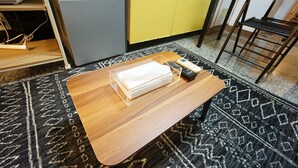 Uma pequena mesa de madeira com um organizador de plástico transparente, um controle remoto e um livro.