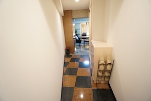 A hallway with a checkered floor, a trash bin, and a seating area with chairs.