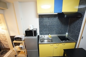 A compact kitchen with a microwave, kettle, sink, and a small refrigerator.