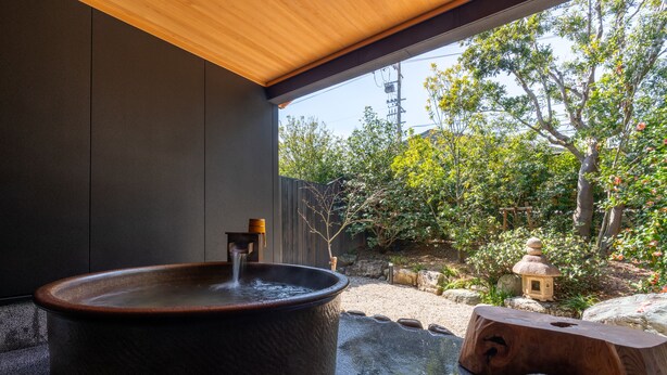 A hot tub in a covered outdoor area with a view of a garden and a small pagoda. - Auberge Yusura (Ise)