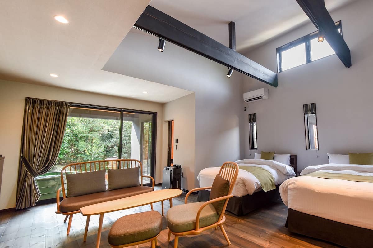 A modern bedroom with two beds, a sofa, a table, and large windows.