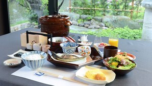 A table set with various dishes, including a bowl of rice, a plate of fish, and a salad, with a view of greenery outside. - Auberge Yusura (Ise)