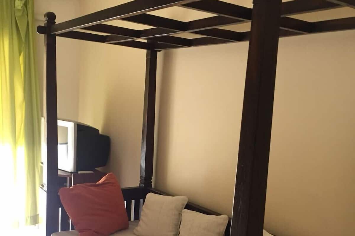 A four-poster bed with a beige mattress and pillows, a television in the corner, and a green curtain.