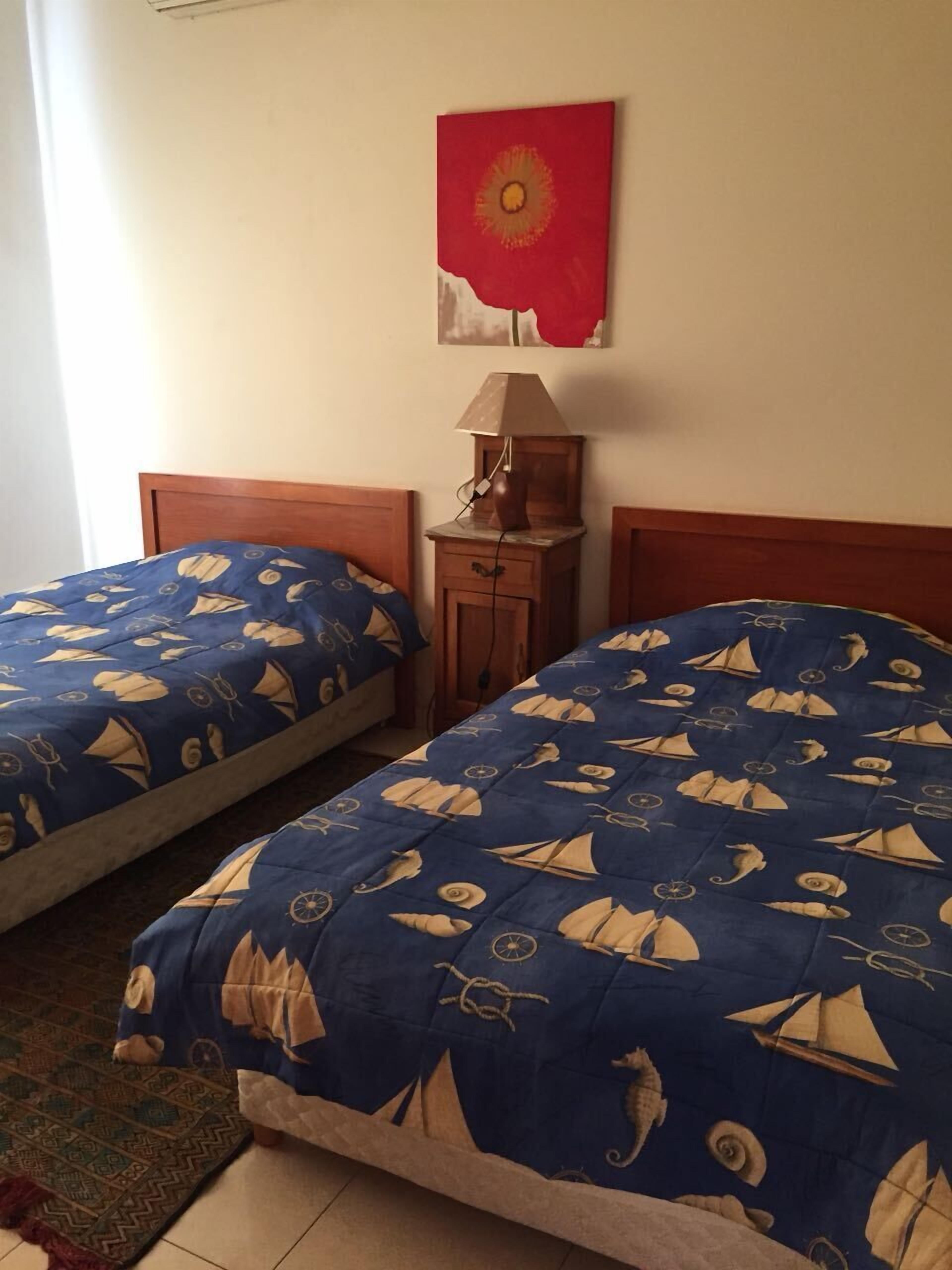 Una habitación con dos camas, una mesita de noche, una lámpara y una obra de arte en la pared.